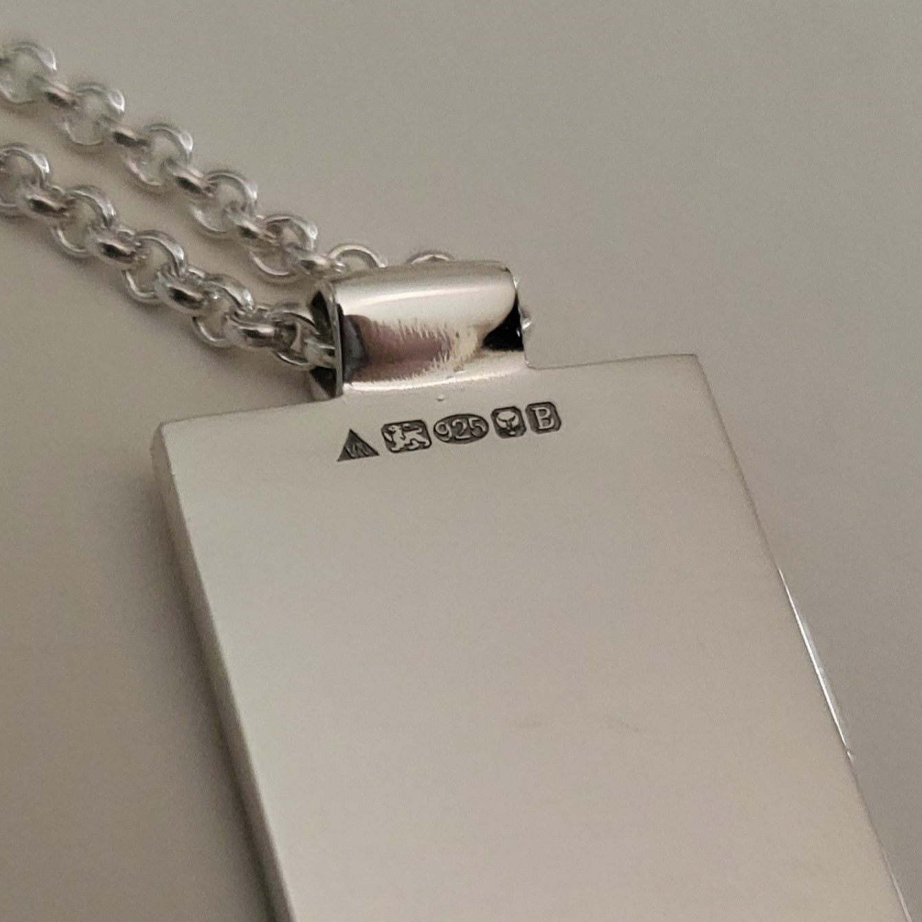 Close-up of the back of silver pendant showing full UK hallmarking with chain on a neutral background