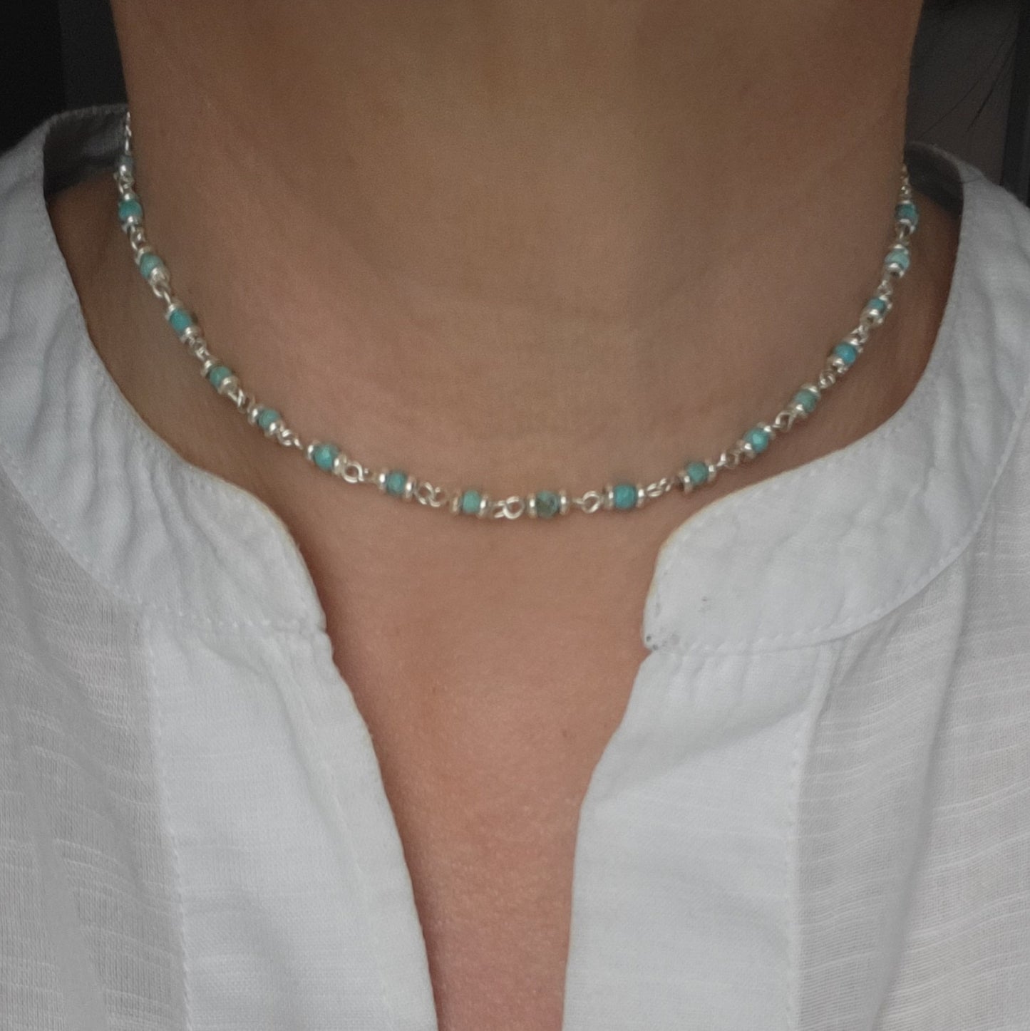 Choker necklace with turquoise beads and silver chain worn by a person in a white shirt.