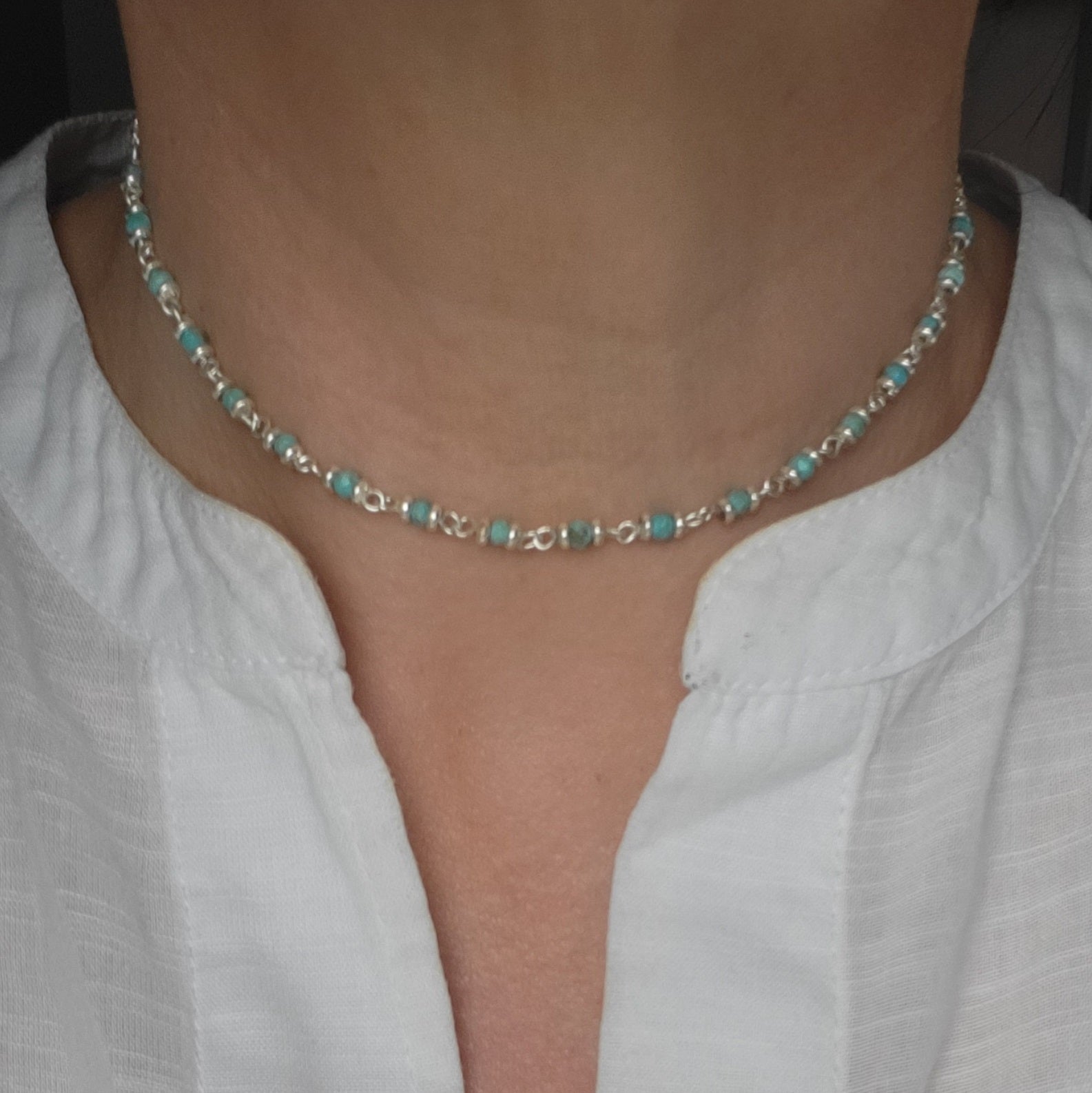 Choker necklace with turquoise beads and silver chain worn by a person in a white shirt.