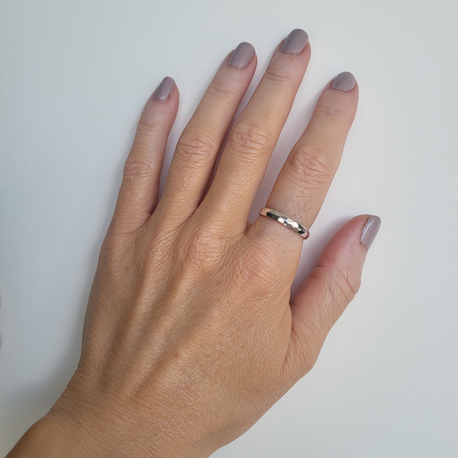 Hand wearing a silver  band ring on a plain background