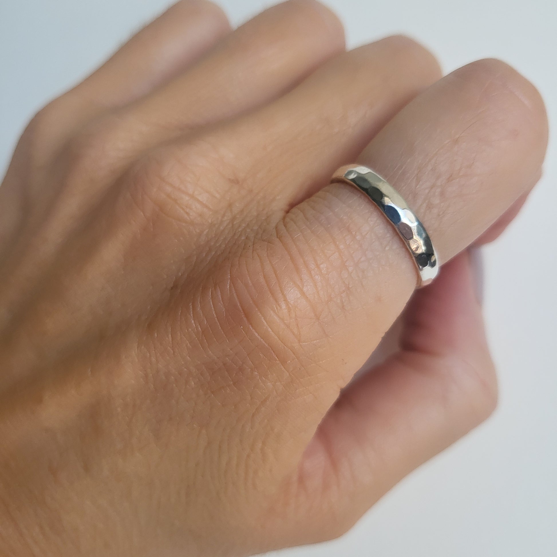 Hammered silver band ring on a person's finger against a white background