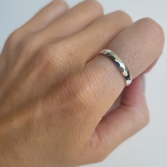 Hammered silver band ring on a person's finger against a white background