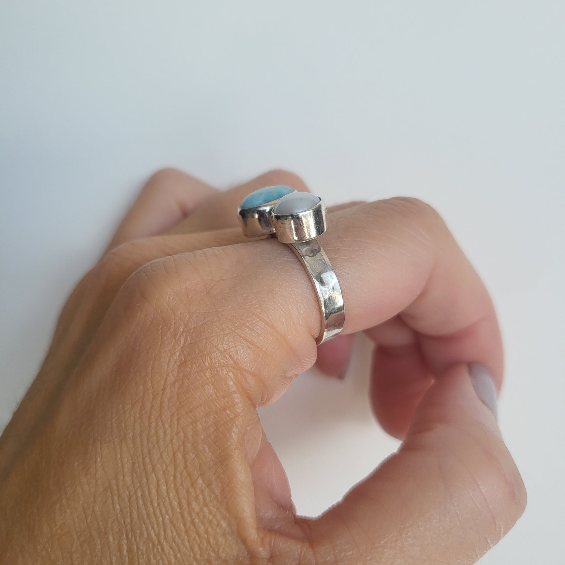 Close up of a hand wearing a silver ring with pearl and larimar stone on a white background