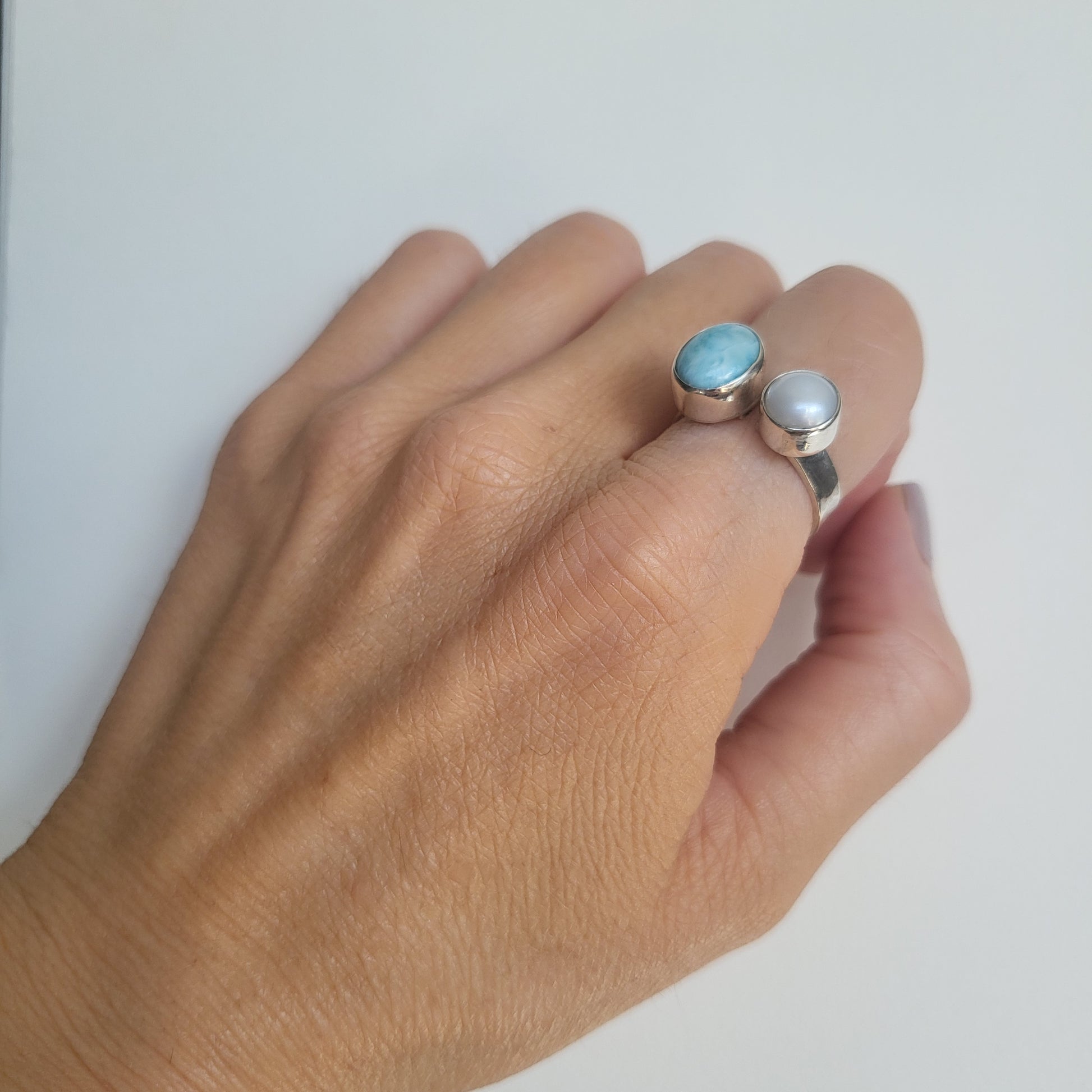 Hand wearing a ring with larimar and pearl gemstones on a light background