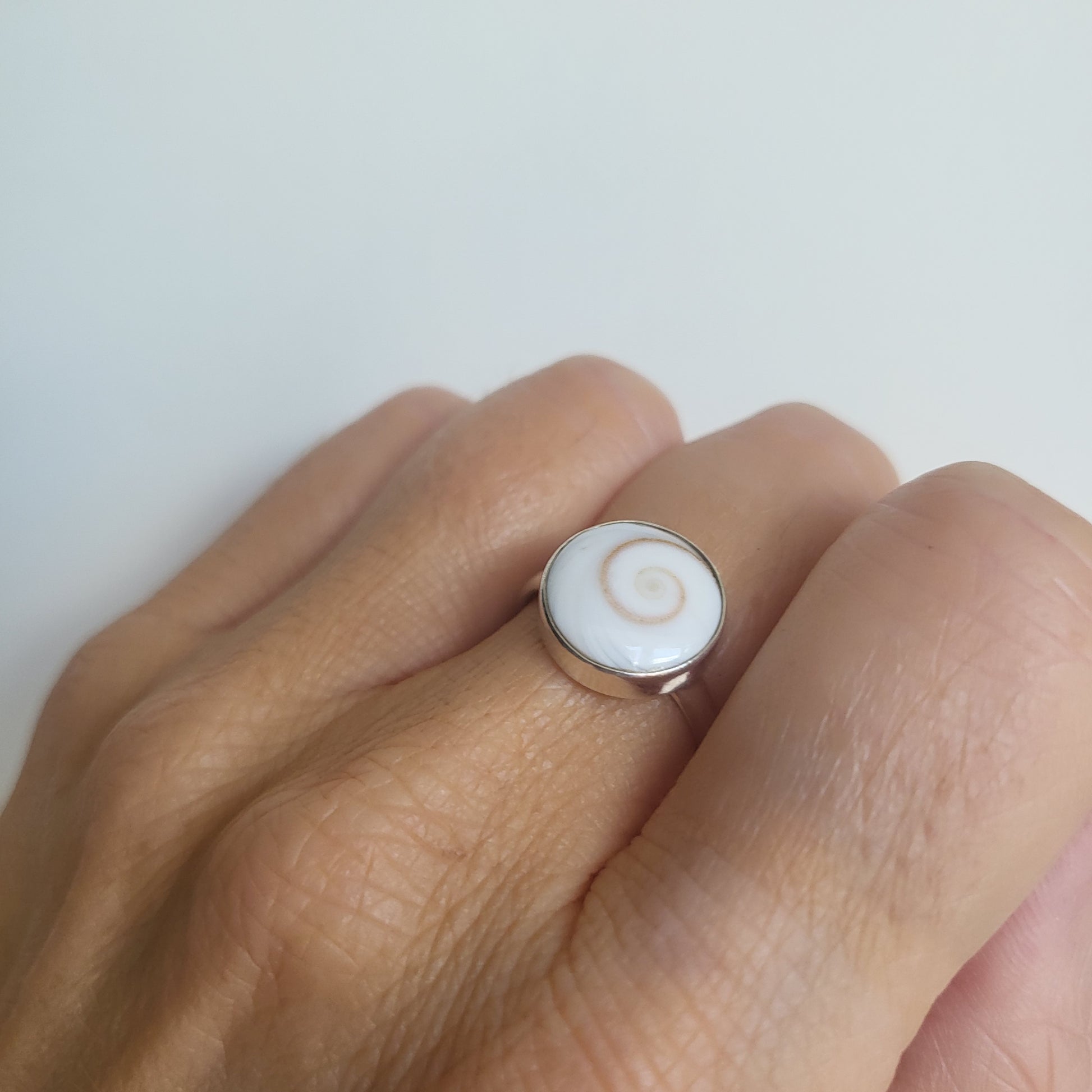 Close-up of a hand wearing a ring with a circular design on a light background