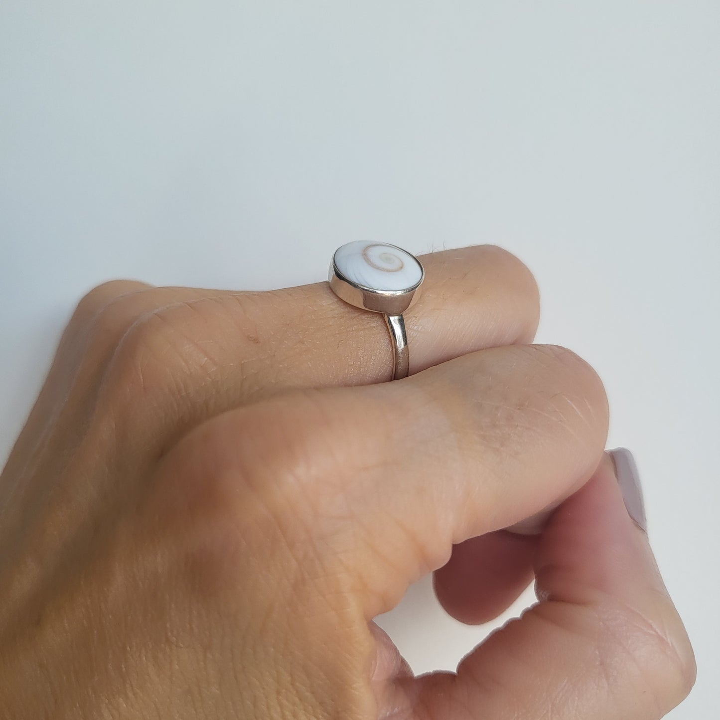 Silver ring with circular shiva shell on a person's finger against a white background