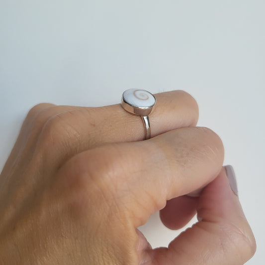 Silver ring with circular shiva shell on a person's finger against a white background