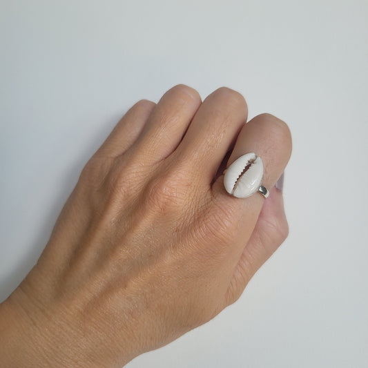 Hand wearing a cowrie shell ring on a plain background