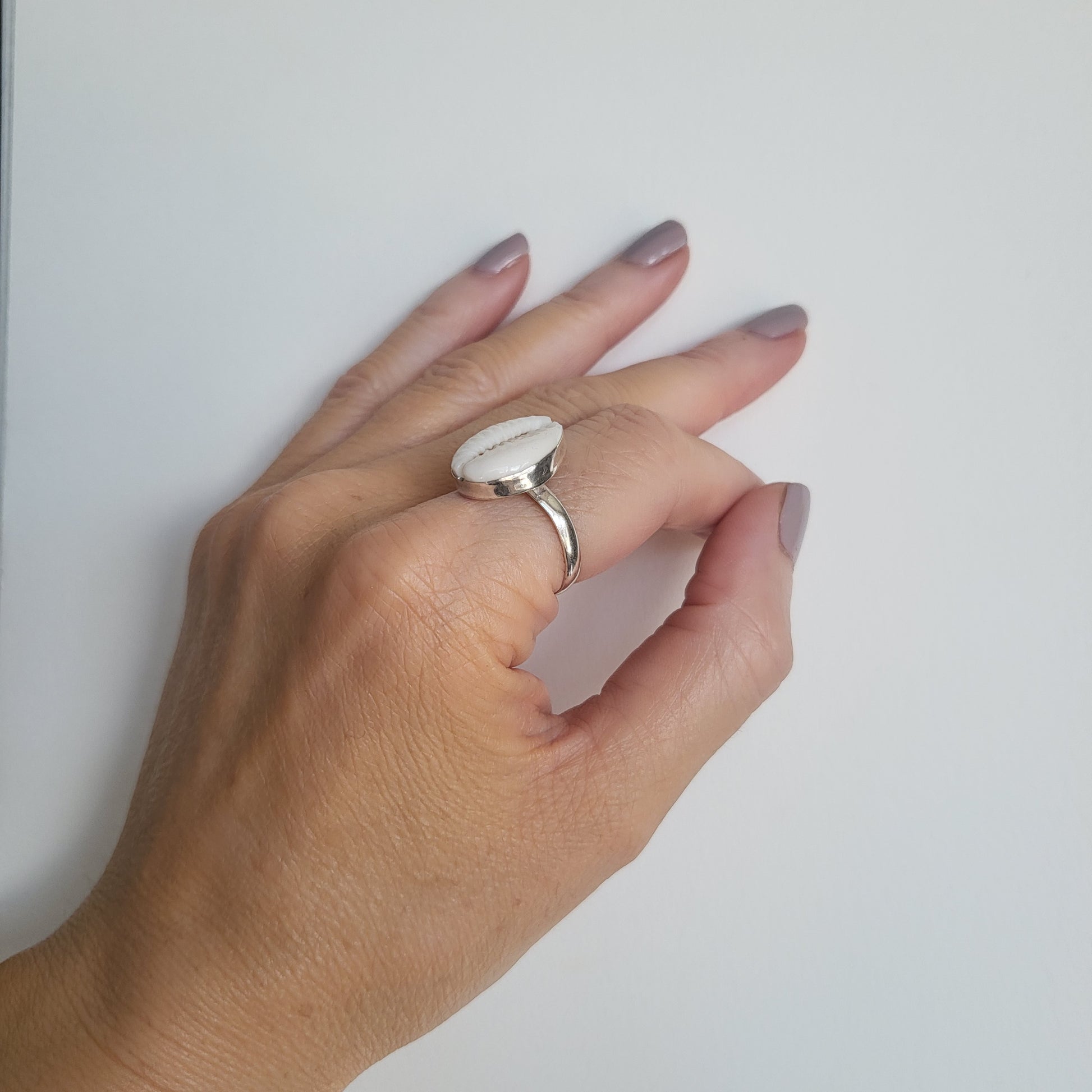 Hand wearing a cowrie shell and silver ring on a light background