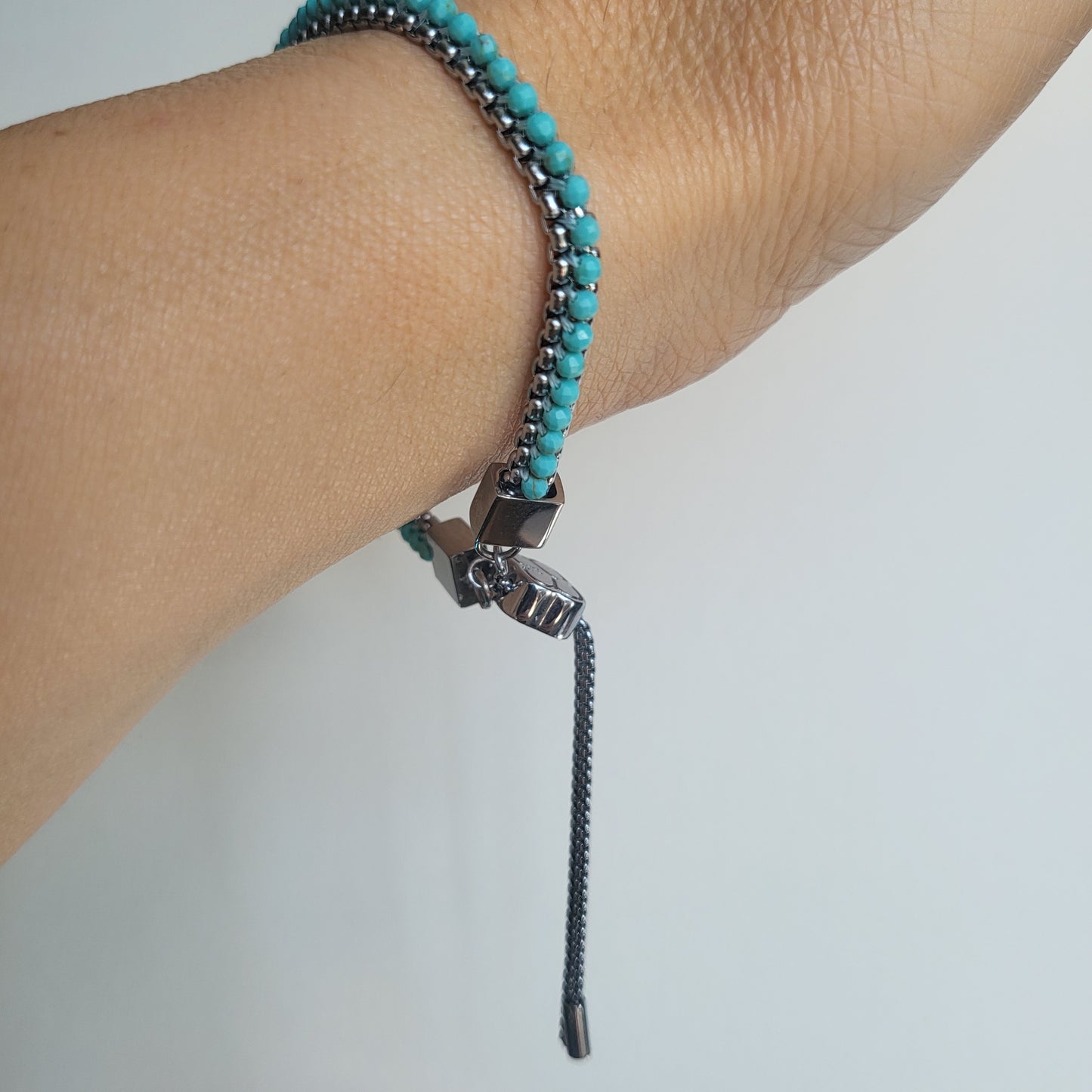 Turquoise and silver adjustable beaded bracelet on a wrist against a plain background
