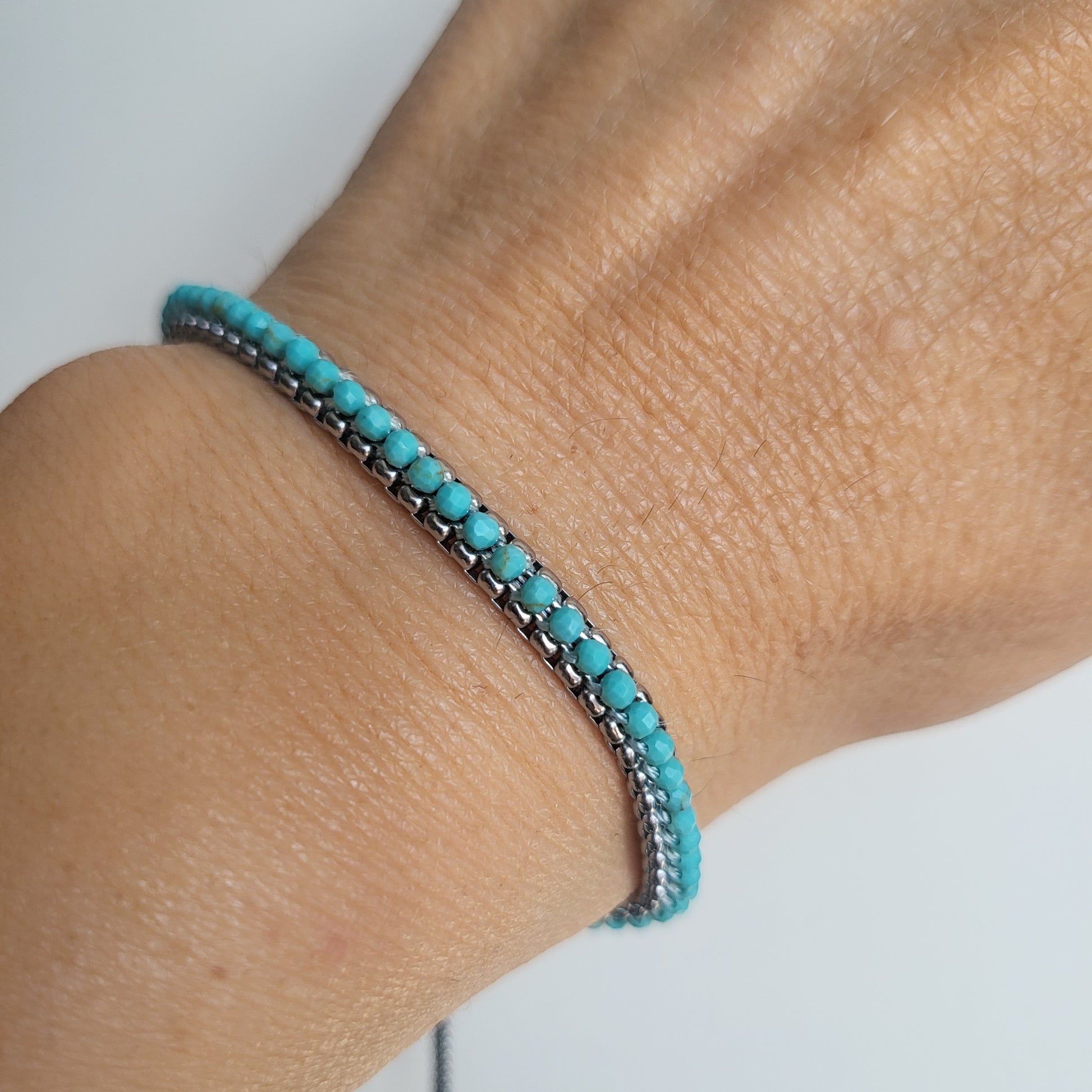 Turquoise and silver beaded bracelet on a wrist against a neutral background