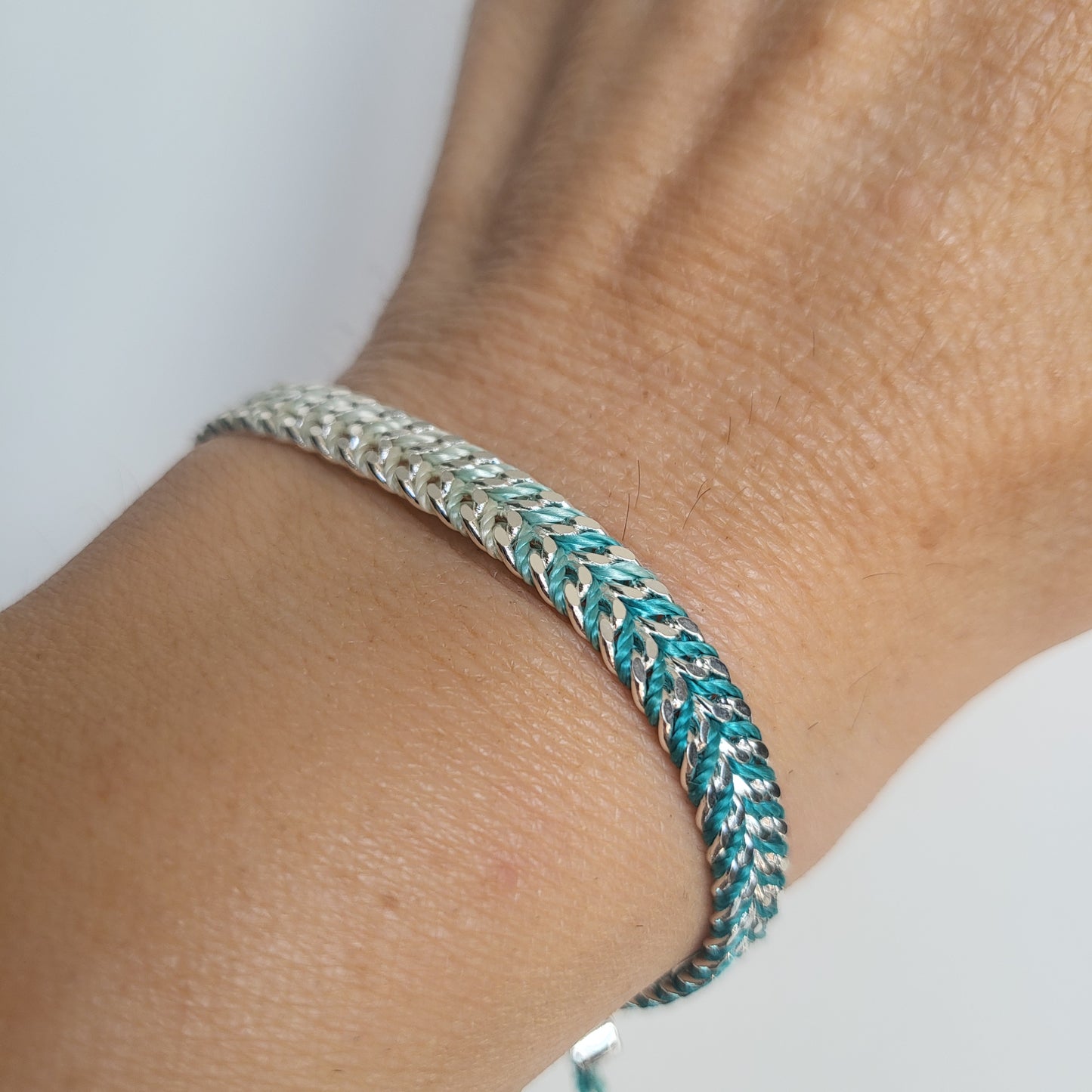 Close-up of a braided silver bracelet on a wrist with a plain background