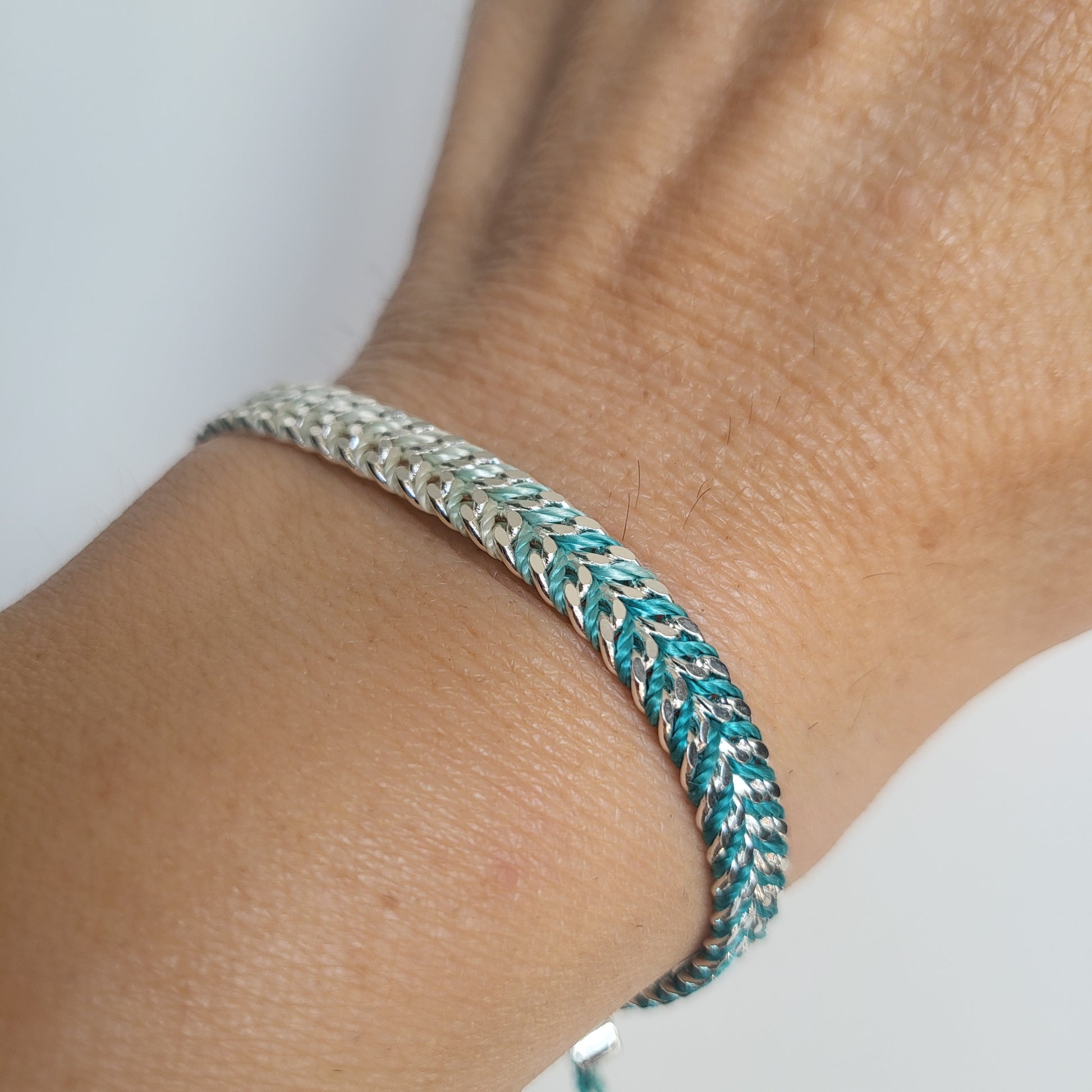 Close-up of a braided silver bracelet on a wrist with a plain background