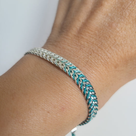 Close-up of a braided silver bracelet on a wrist with a plain background