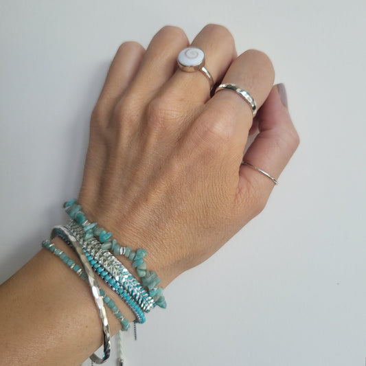 Hand wearing multiple bracelets and rings on a plain background