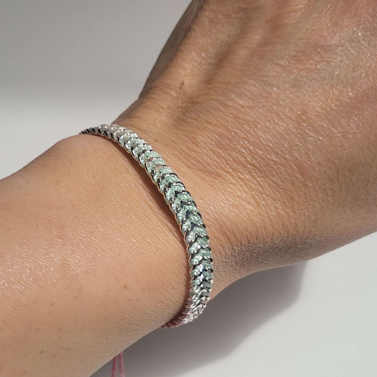 Close-up of a braided silver bracelet on a wrist against a neutral background