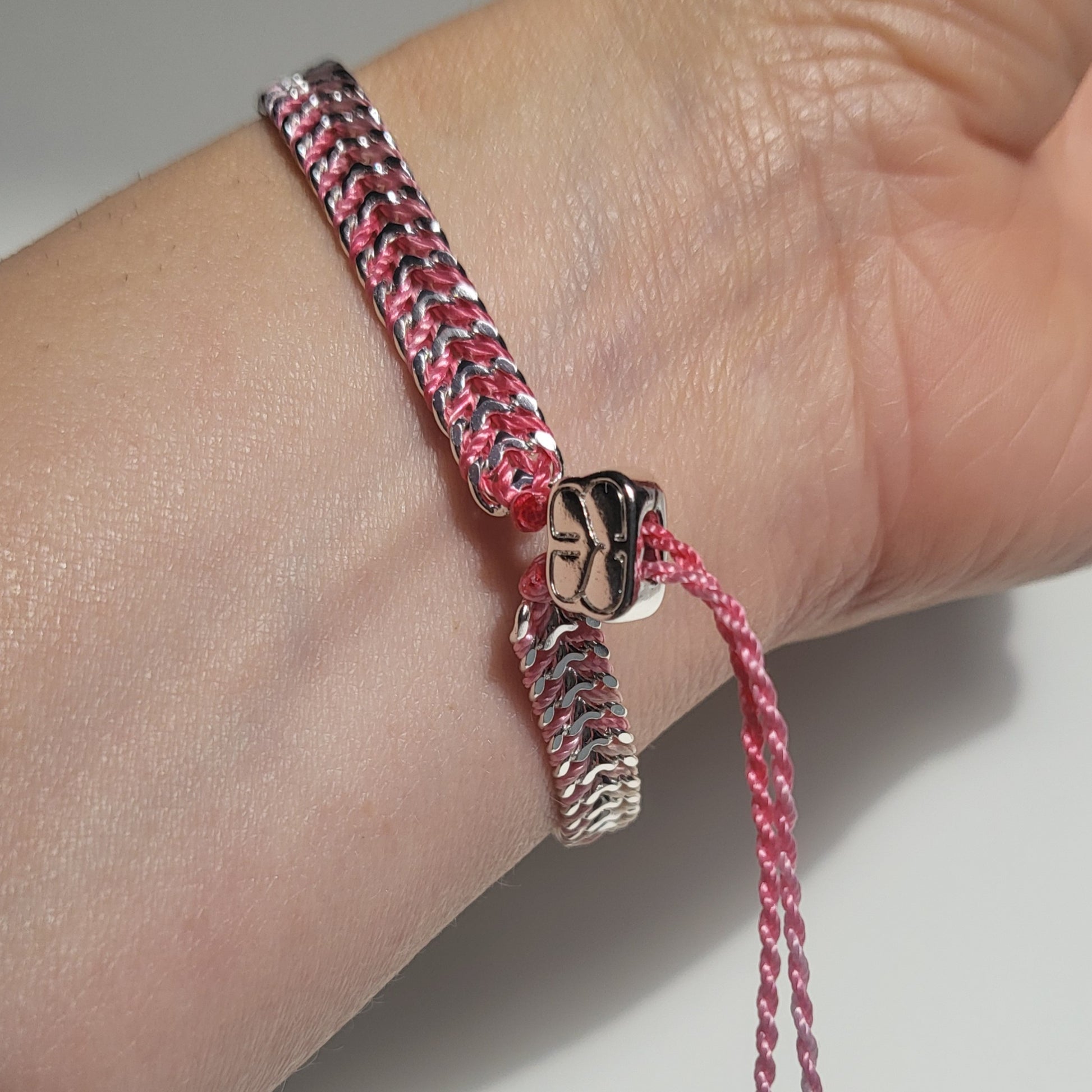 Bracelet with pink and silver braided design on a wrist against a neutral background