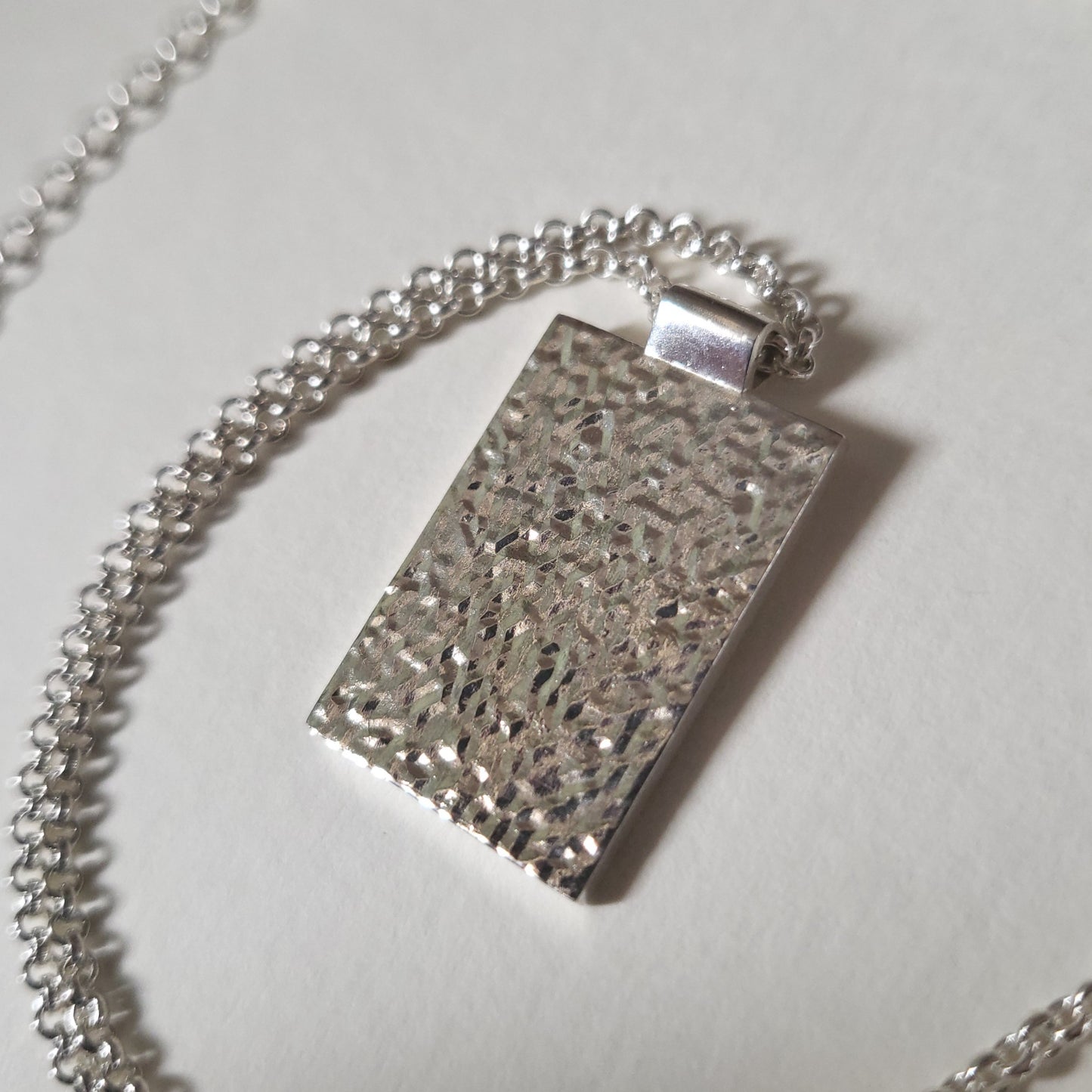 Silver textured pendant on a chain against a light background