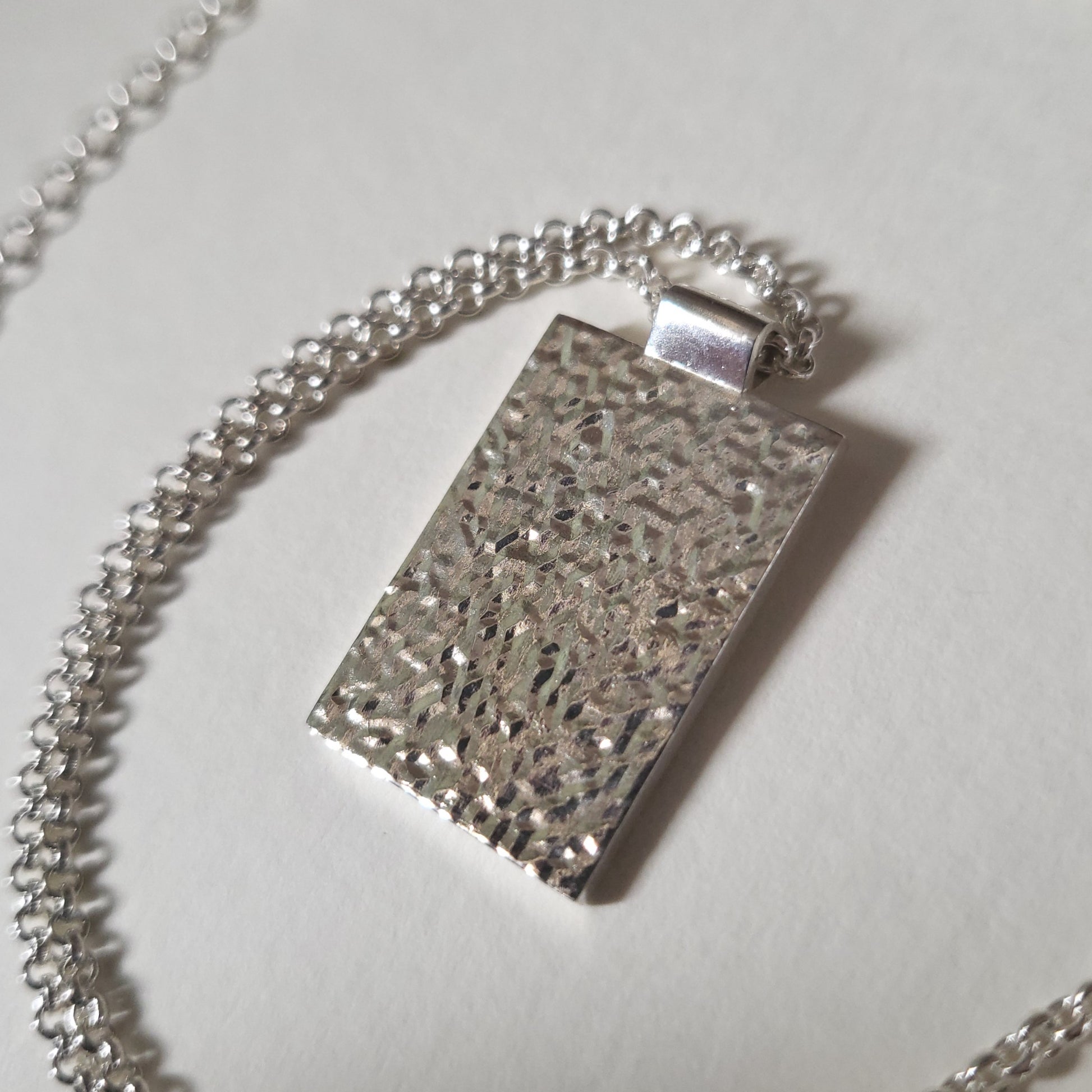 Silver textured pendant on a chain against a light background
