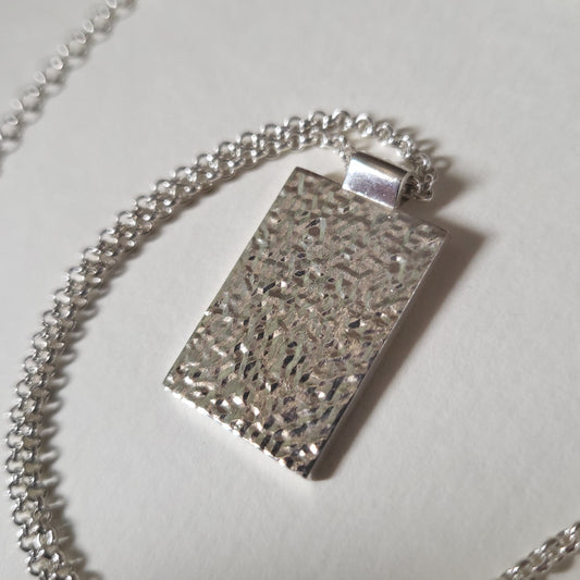Silver textured pendant on a chain against a light background