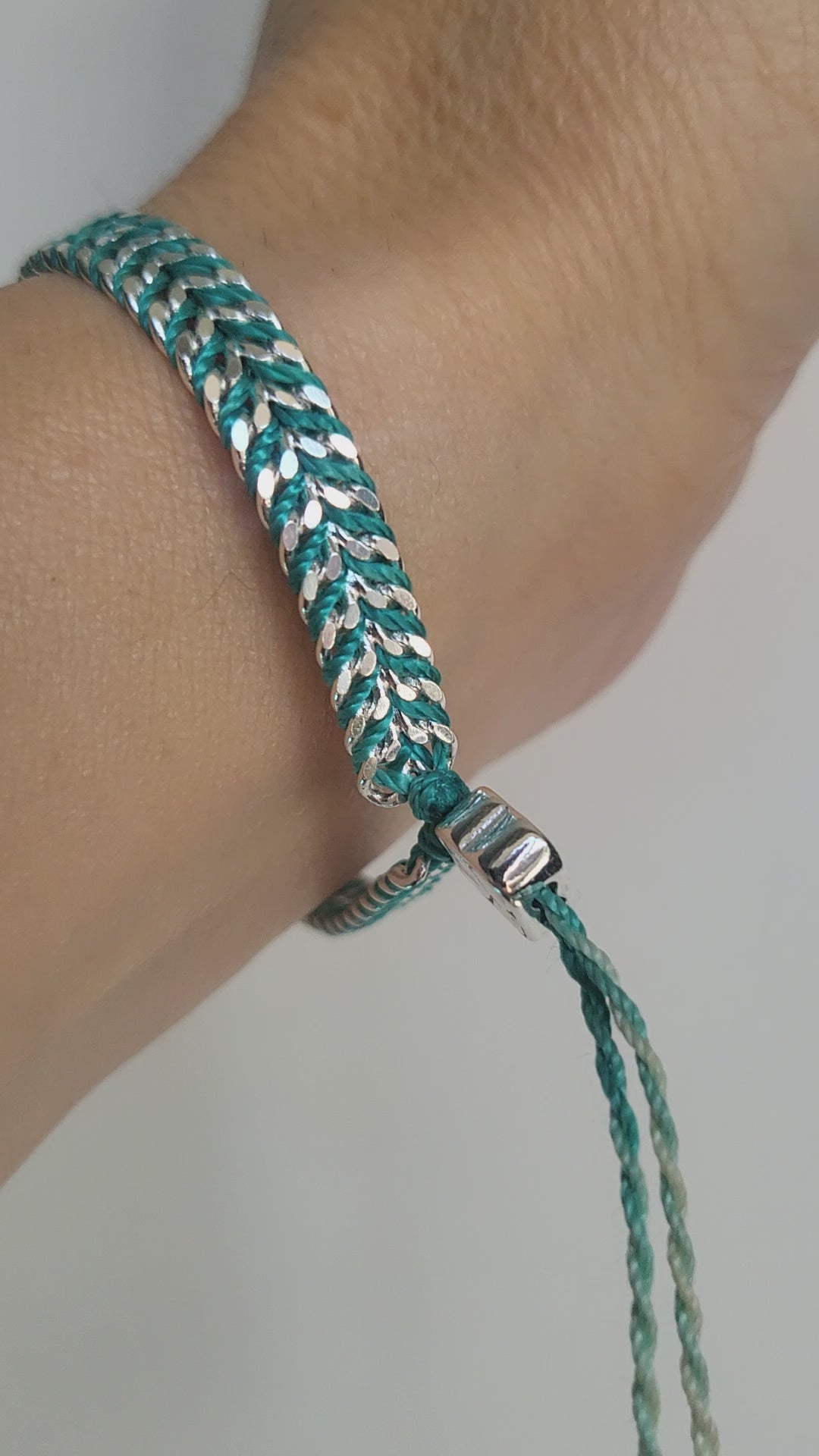 Video of a silver and turquoise braided adjustable bracelet on a wrist against a white background