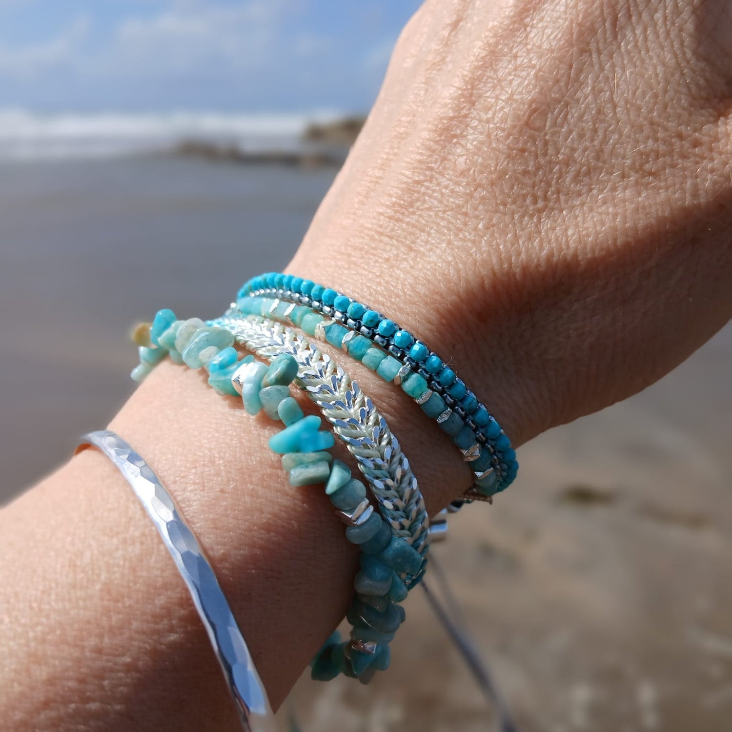 Close-up of silver and Amazonite stacking bracelets from the Salt and Sky Collection, showing hammered textures and soft green-blue stones on a sun-kissed wrist.